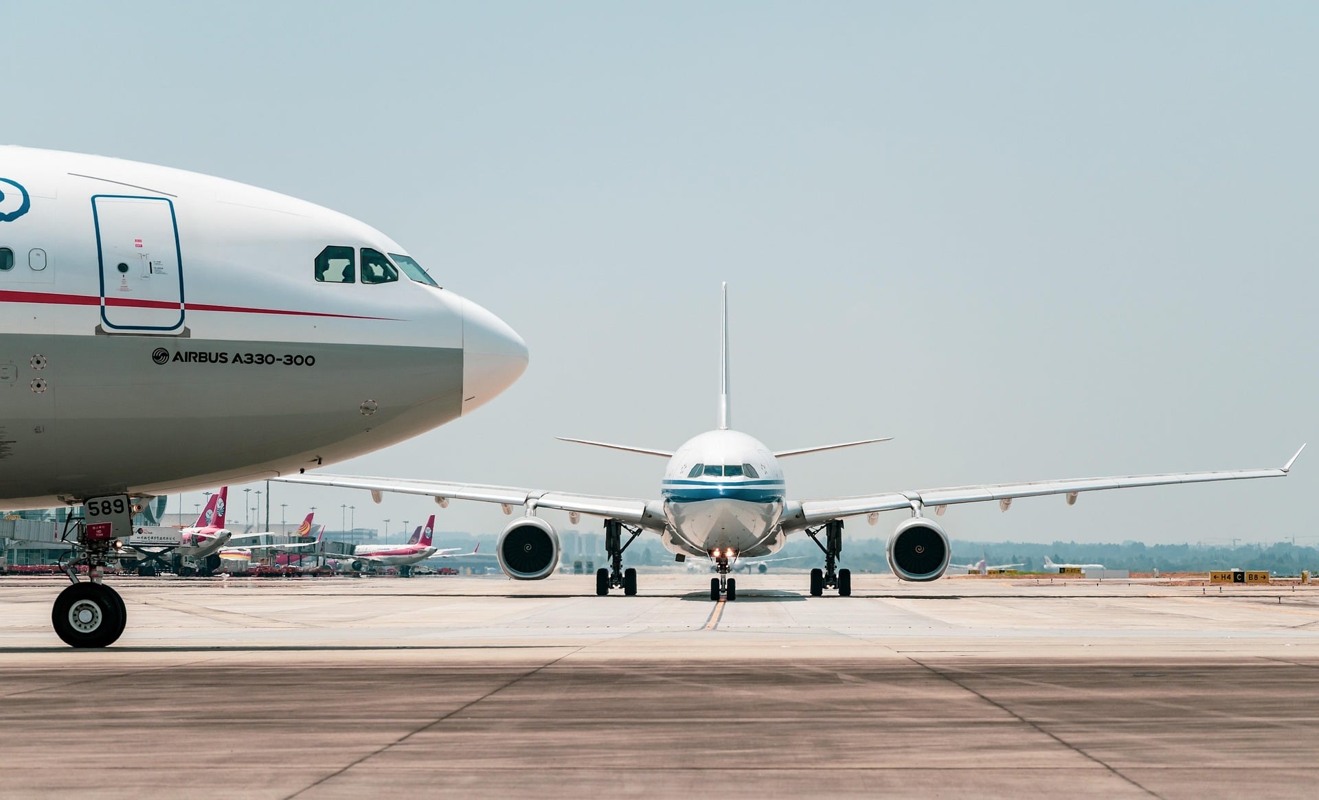 Frontansicht eines Passagierflugzeugs, das auf der Start- und Landebahn rollt, mit einem großen Airbus-Flugzeug links geparkt und weiteren Flugzeugen im Hintergrund.