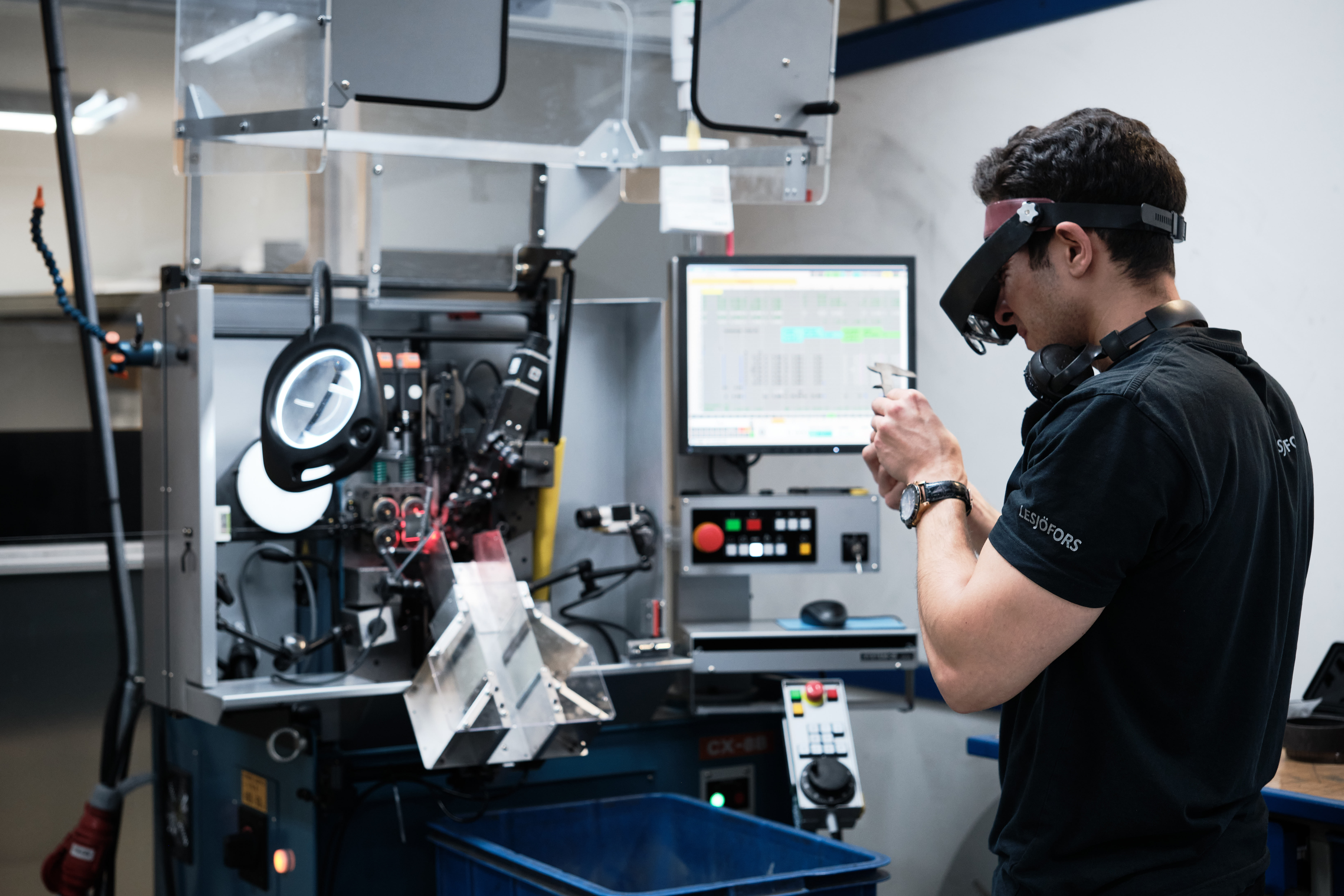 Eine Lesjöfors-Mitarbeiterin oder ein Lesjöfors-Mitarbeiter prüft ein kleines Metallteil an einer Präzisionsfertigungsmaschine.