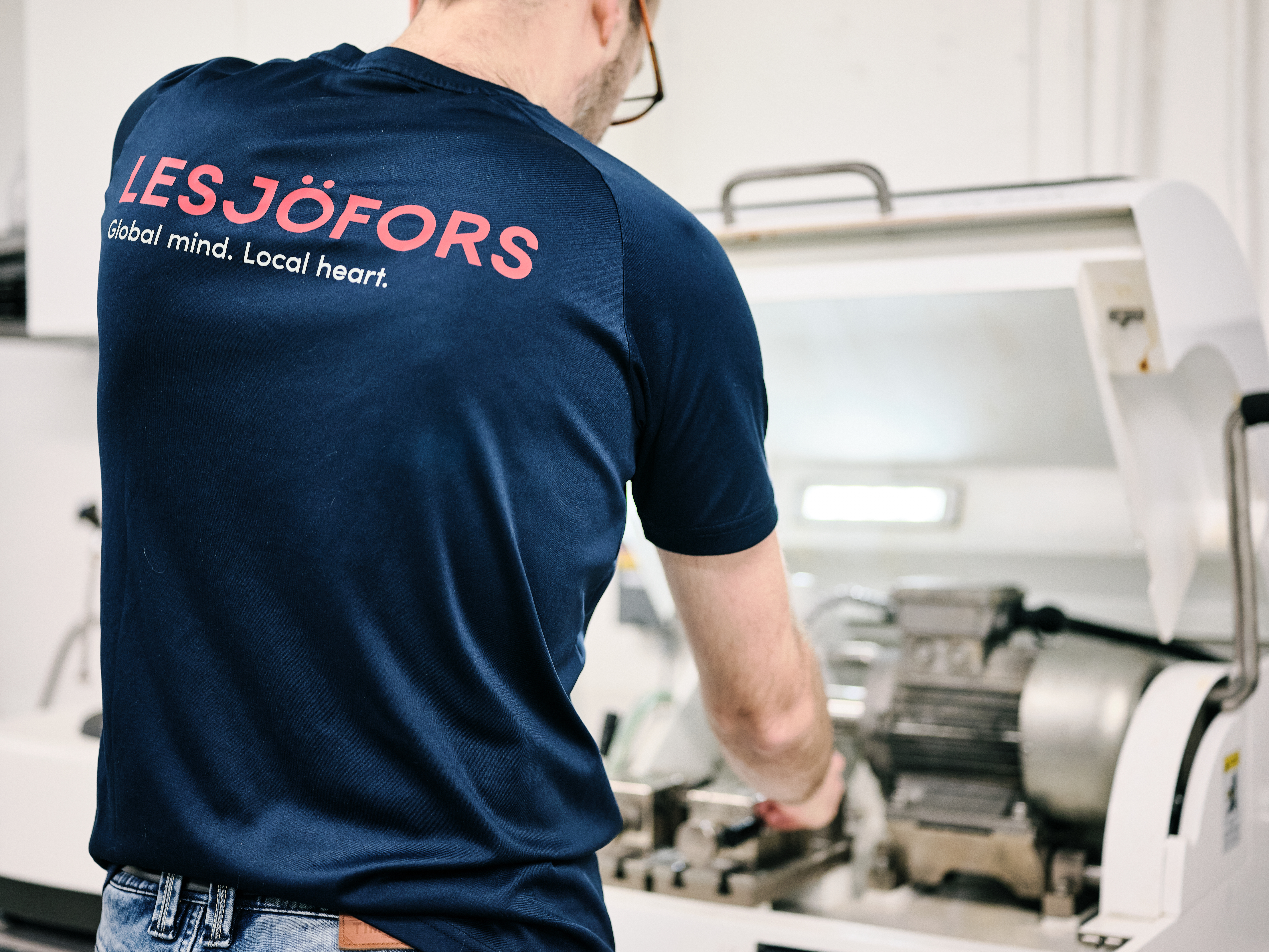 Eine Lesjöfors-Mitarbeiterin oder ein Lesjöfors-Mitarbeiter ist von hinten zu sehen und bedient Maschinen in einer Werkstatt.