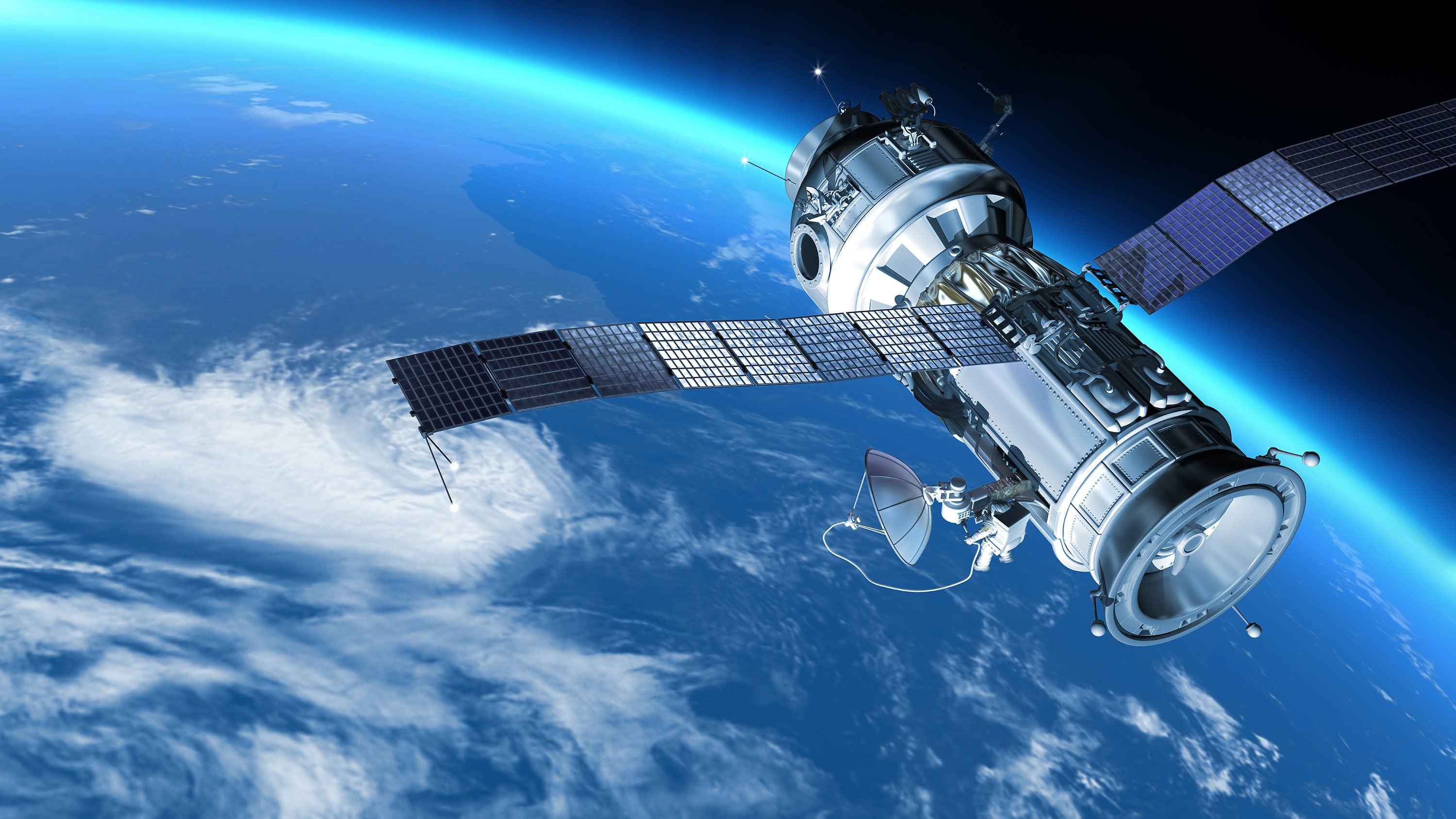 Ein Satellit mit großen Solarpaneelen umkreist die Erde. Darunter sind weiße Wolken und leuchtend blaue Ozeane zu sehen.