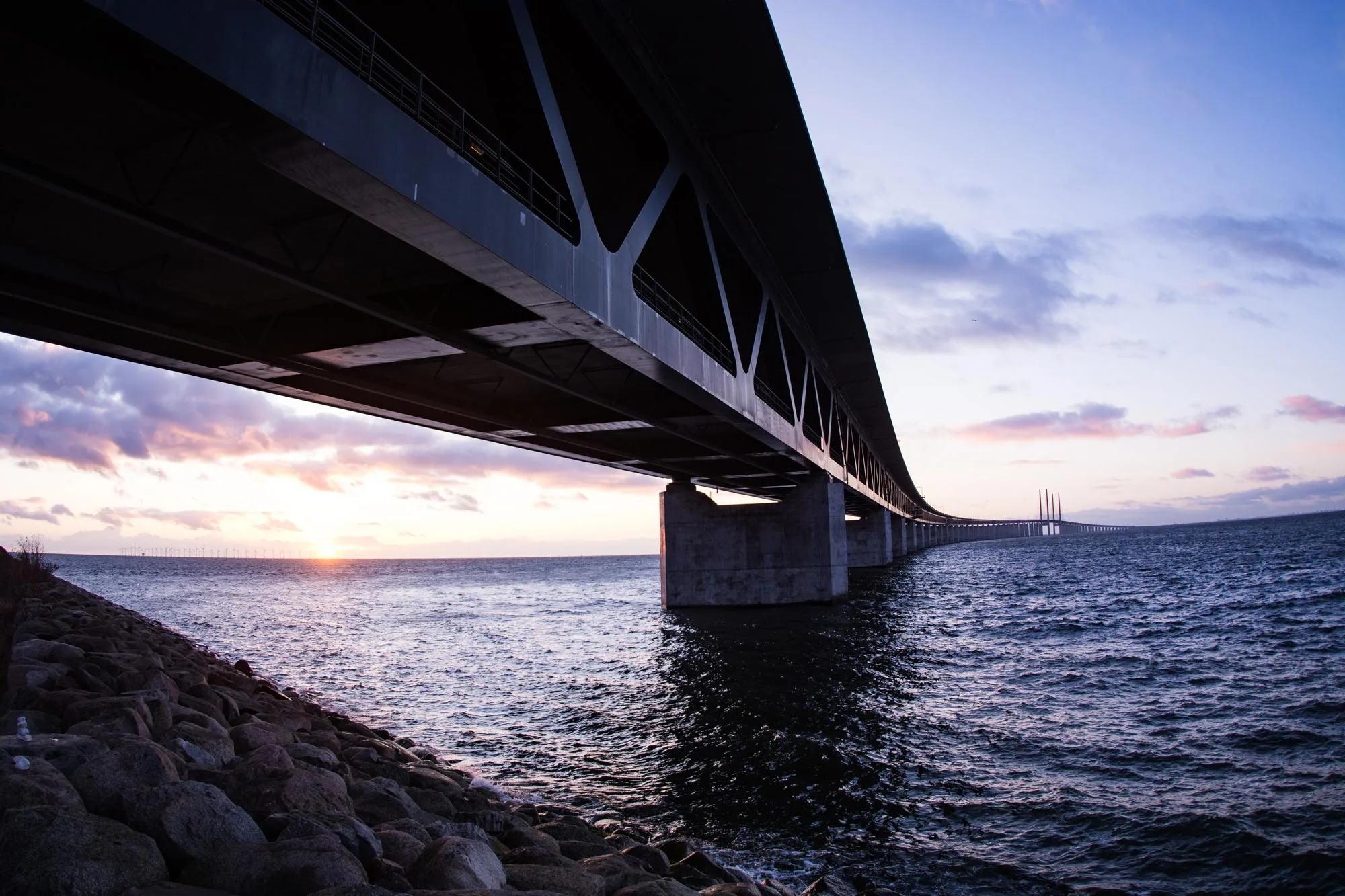 Underside view of the Öresund Bridge spanning open water at dusk, highlighting the scale and structure of this major piece of bridge infrastructure.