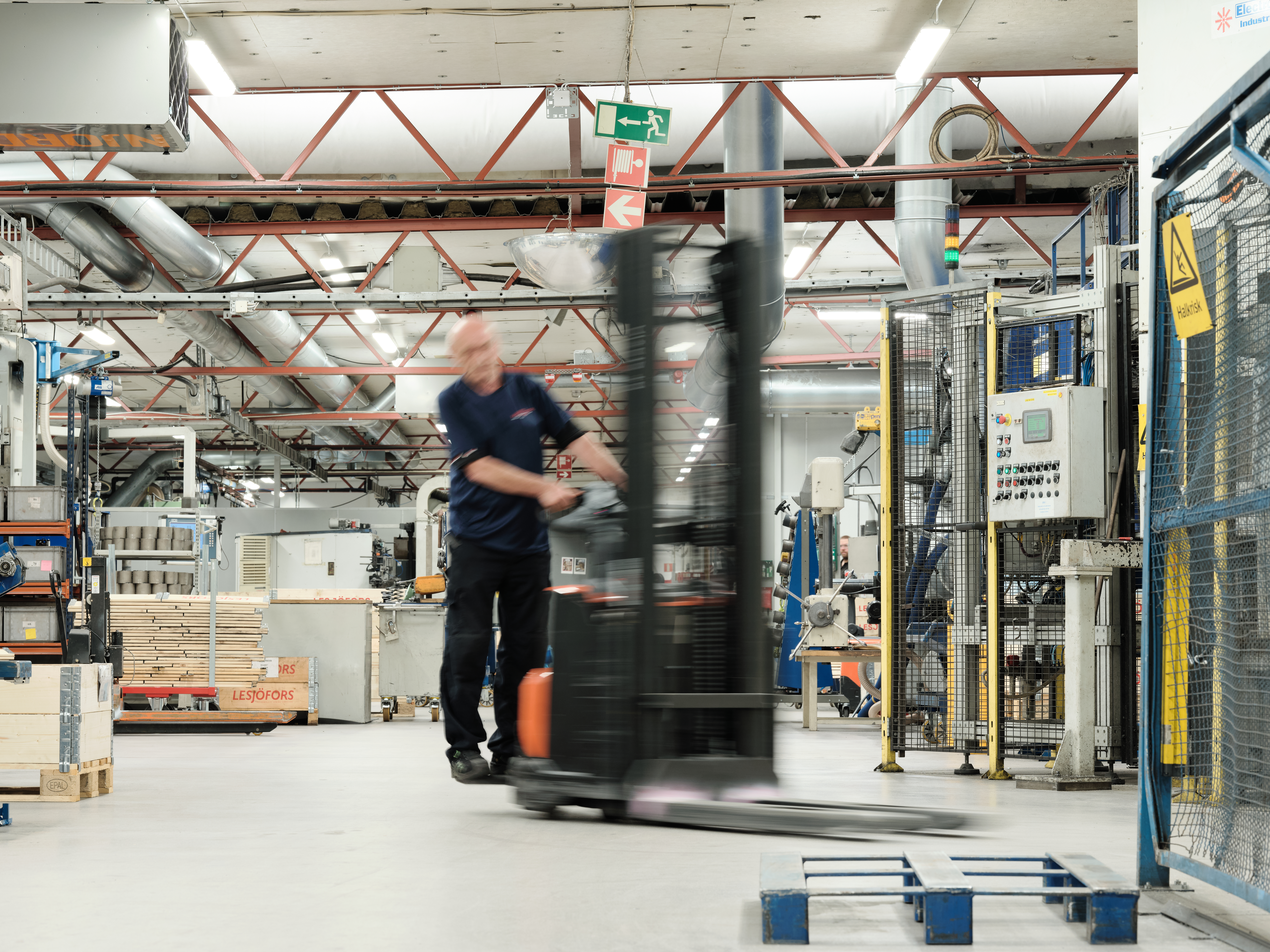 Bevegelsesuskarp Lesjöfors-medarbeider som kjører en gaffeltruck inne i et produksjonsanlegg.
