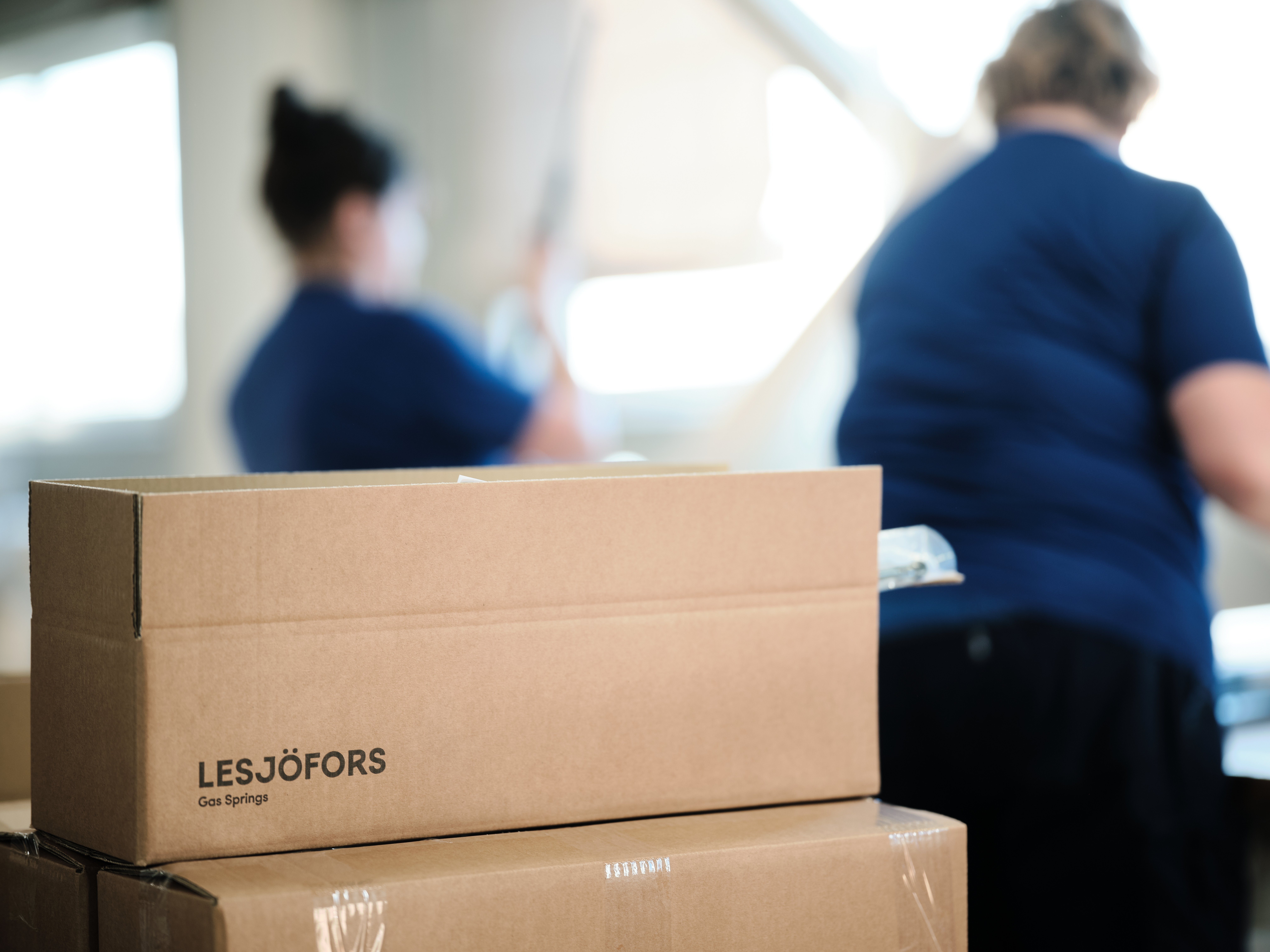 Pappesker som brukes til å pakke og sende Lesjöfors-produkter, med ansatte synlige i bakgrunnen.
