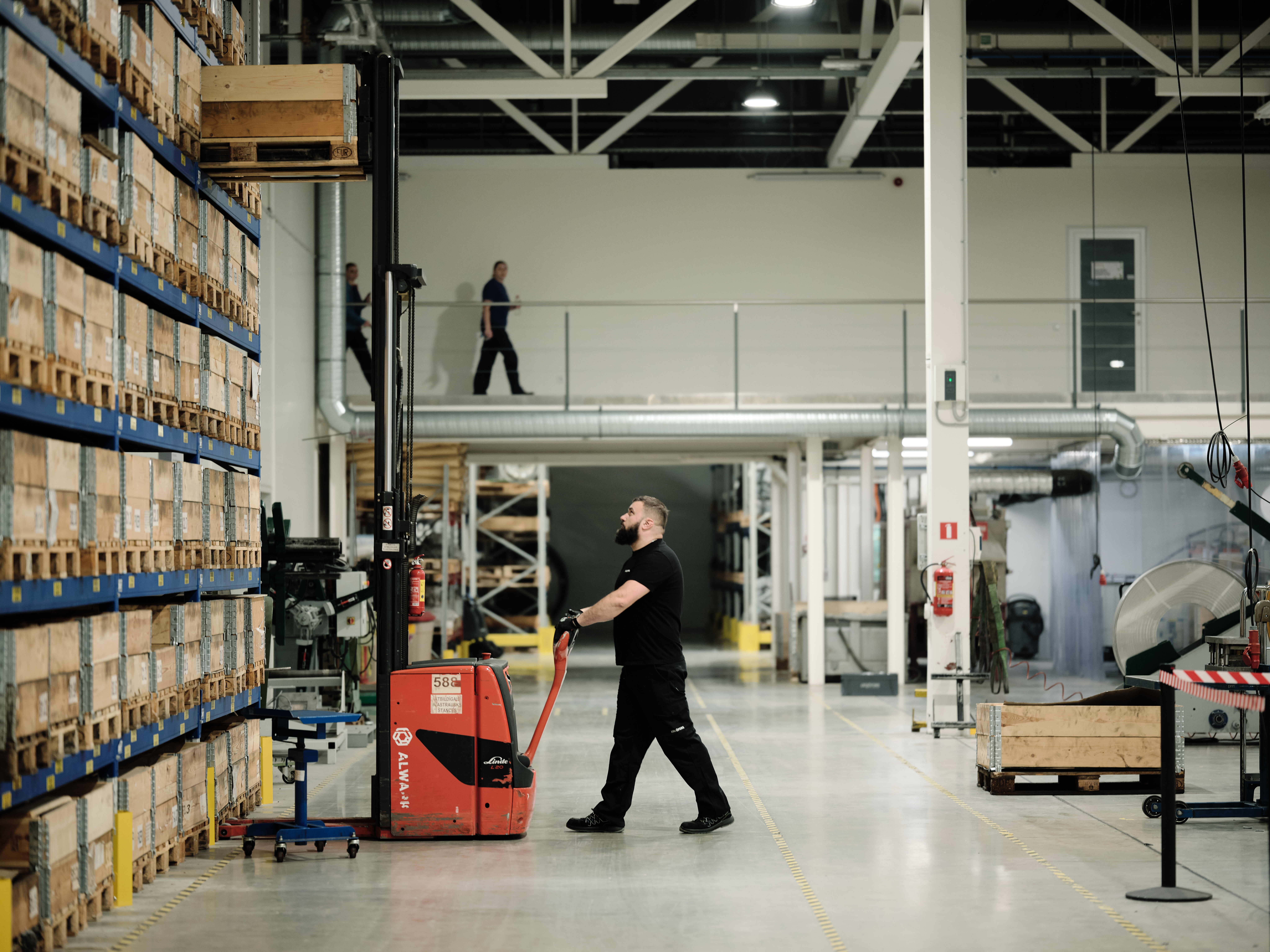 Lesjöfors-medarbeider som kjører en elektrisk palletruck ved siden av rader med stablede trekasser inne i et produksjonsanlegg.