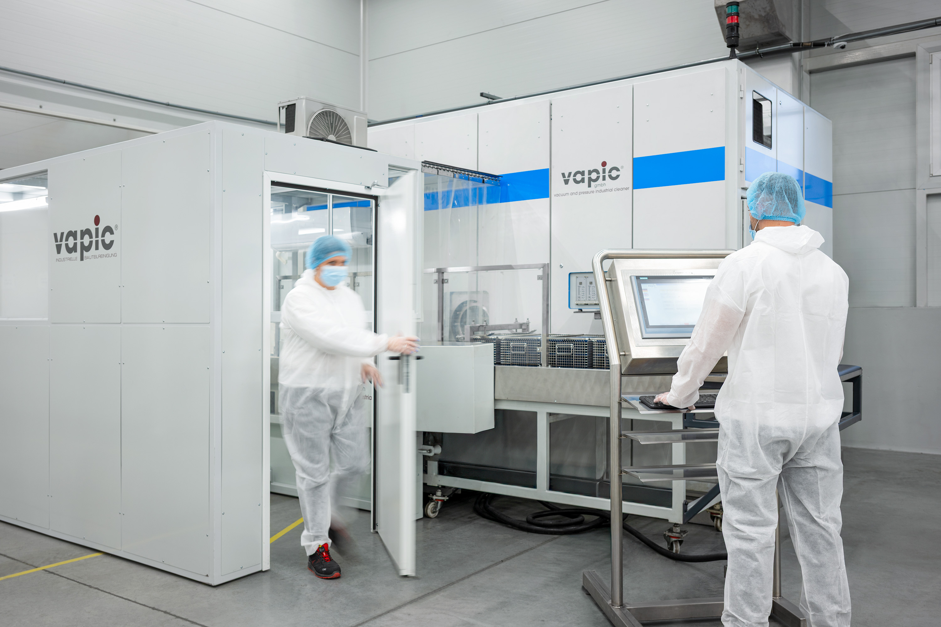 Teknikere i hvide beskyttelsesdragter betjener maskiner i et sterilt, moderne laboratorium.