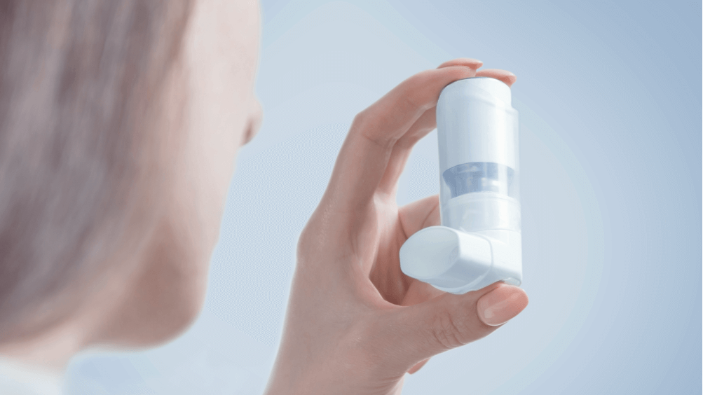 En person holder en hvid inhalator mod en blød blå baggrund. Fokus er på inhalatoren.