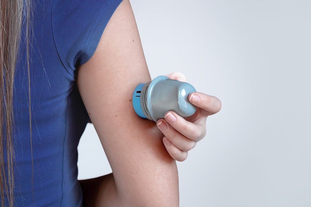 Eine Person in einem blauen Hemd bringt mit einem Handgerät ein kontinuierliches Glukosemesssystem am Oberarm an.