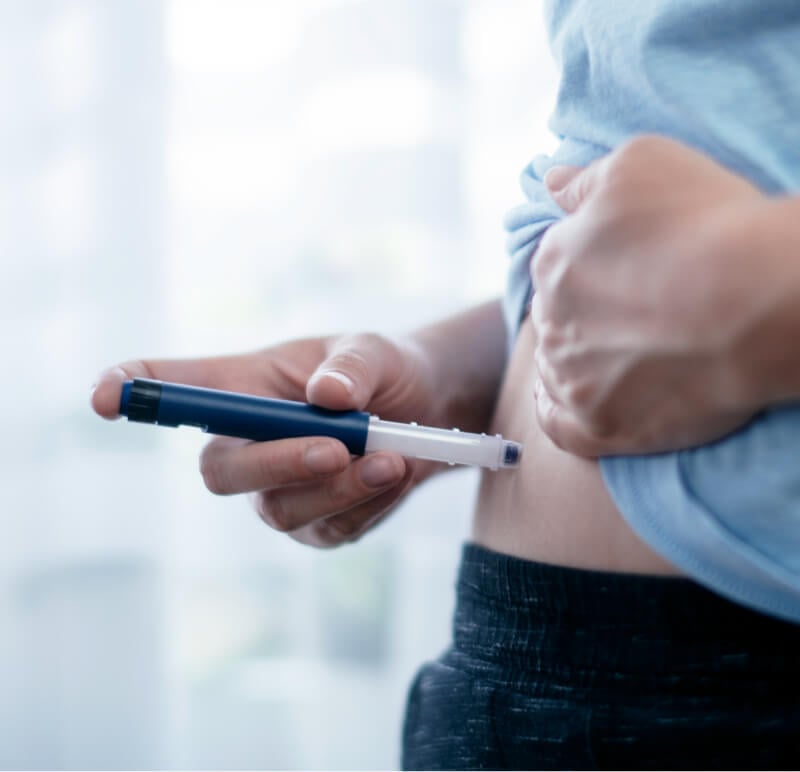 Eine Person verwendet einen Pen-Injektor, um sich eine Insulininjektion in den Bauch zu verabreichen.