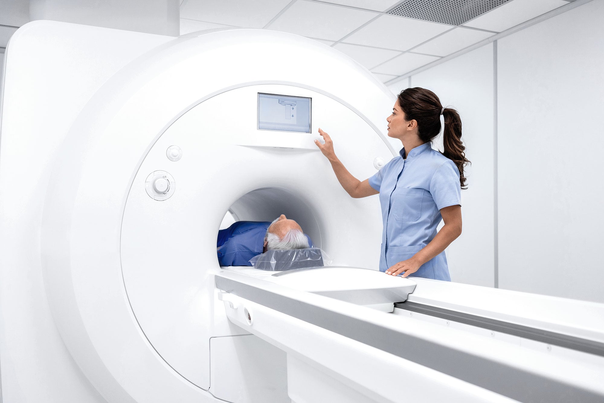 En sundhedsprofessionel betjener en MR-scanner, mens en patient ligger indeni. Miljøet er klinisk og understreger præcision og omhu i et hospitalsmiljø.