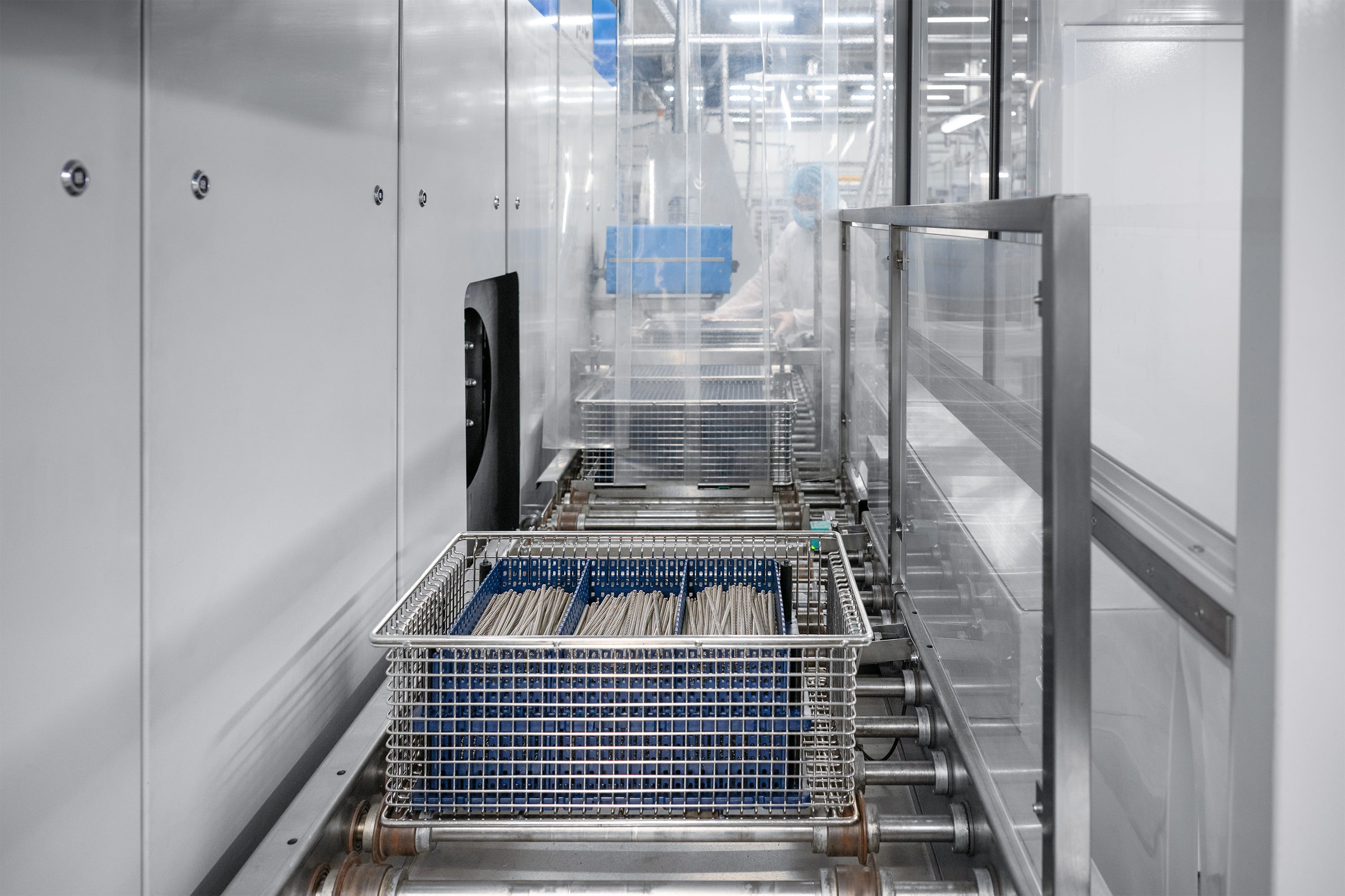 Industrielt miljø med et transportbåndssystem i et stilrent, metallisk design. Omgivelserne er rene og sterile, hvilket antyder et højteknologisk anlæg.