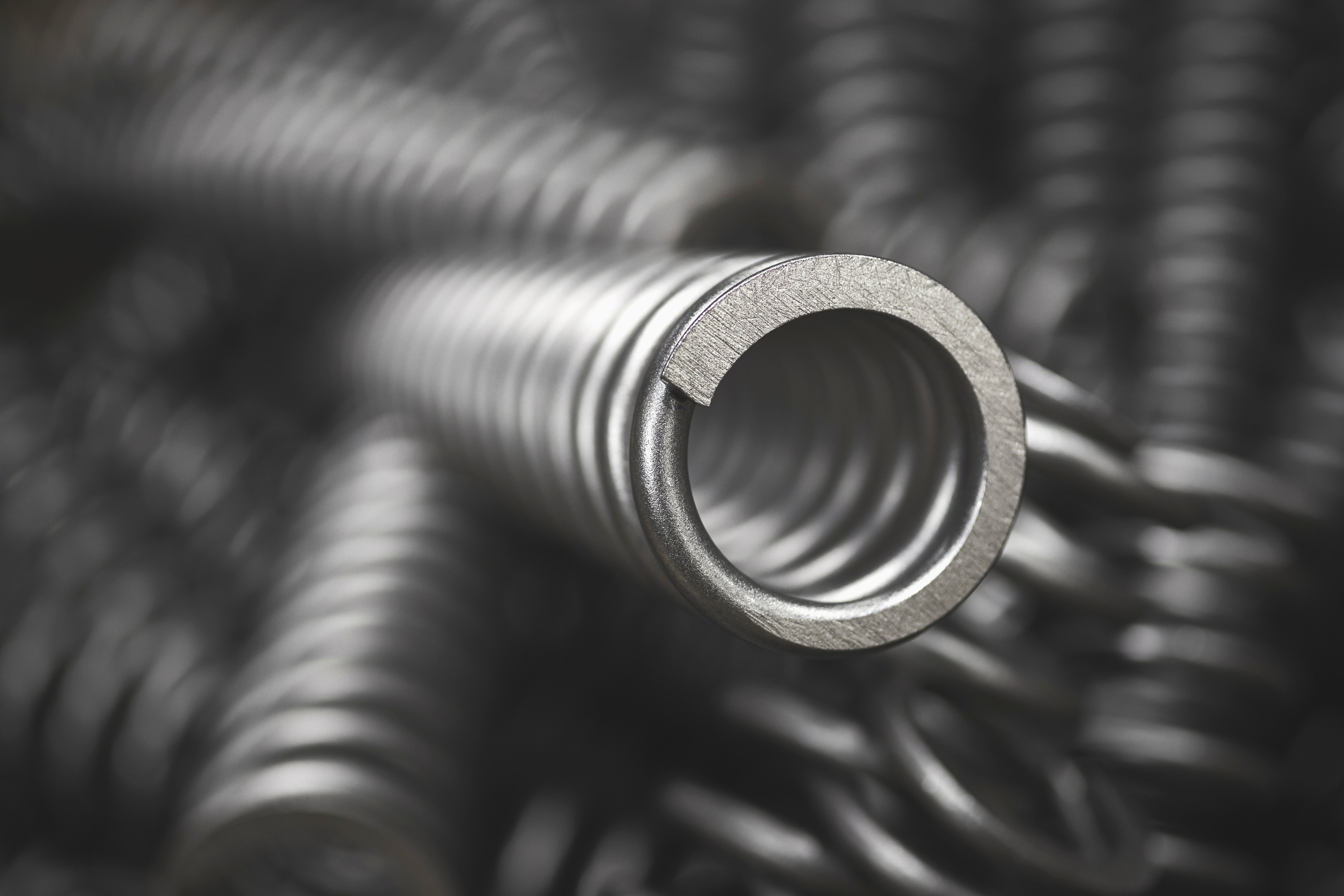 Nårbilde av en blank metallfjær viklet i et spiralformet mønster. Fokuset på fjæren fremhever den glatte overflaten og presise utformingen. Bakgrunnen er uskarp.