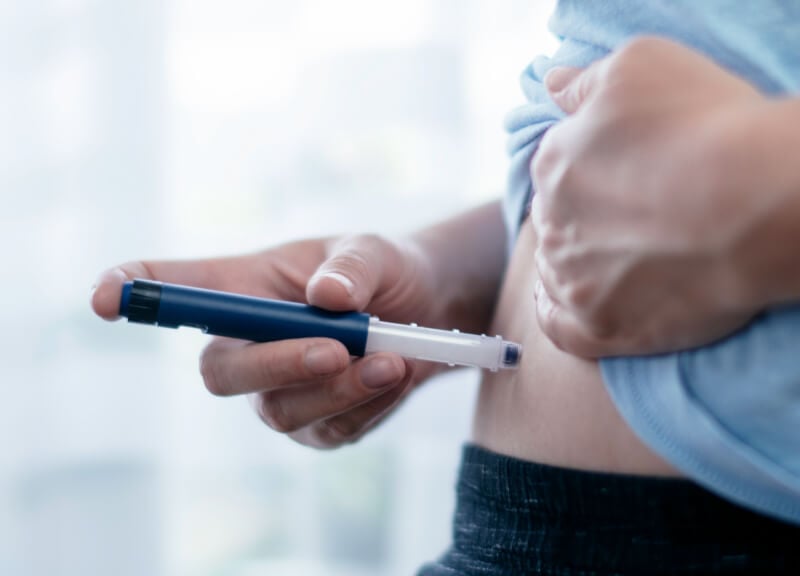 Eine Person verwendet einen Pen-Injektor, um sich eine Insulininjektion in den Bauch zu verabreichen.