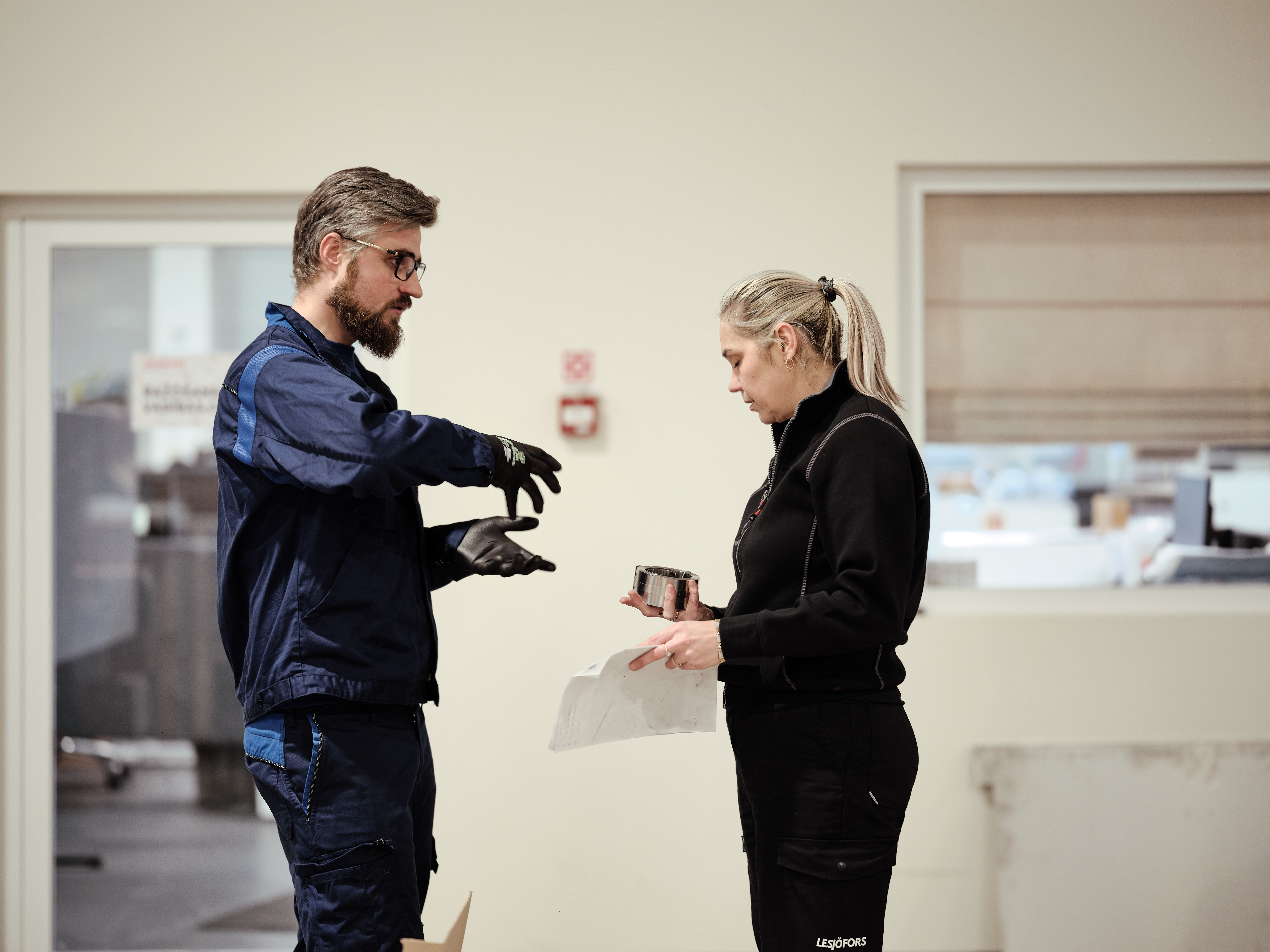 Two workers discussing a metal component in a production environment.