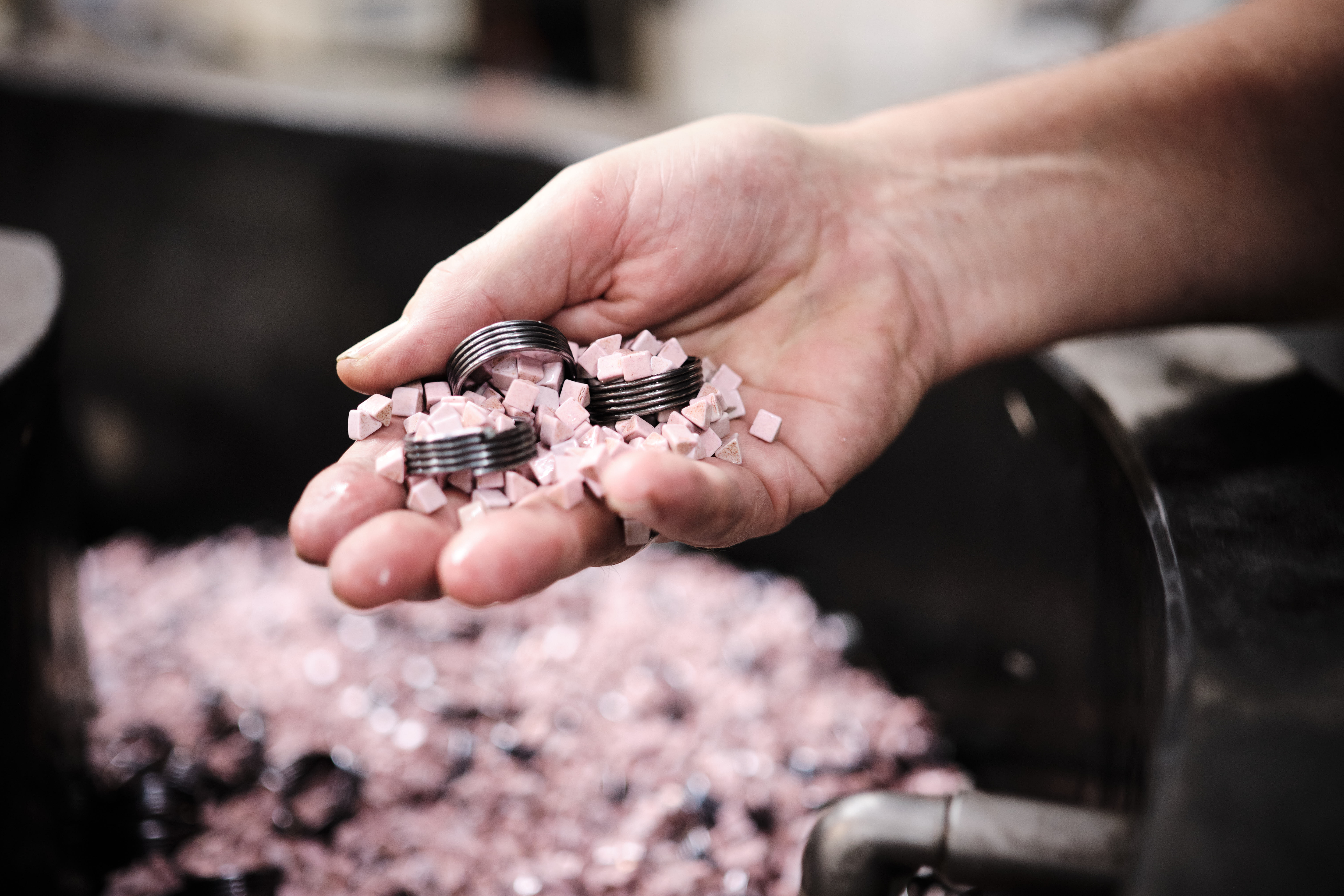 Close-up of a hand holding three metal rings mixed with small pink plastic media over a container filled with the same materials.
