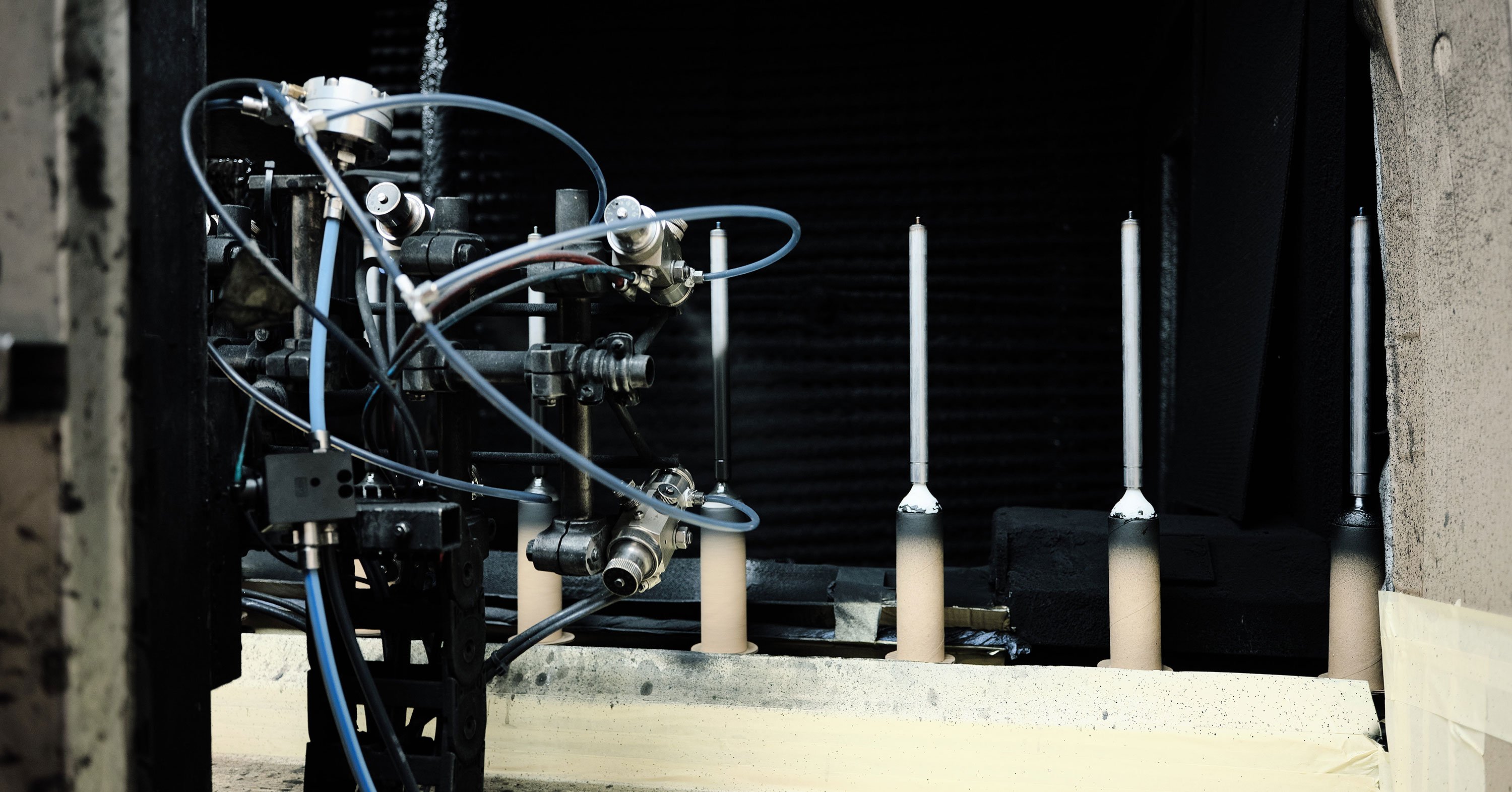Gas spring components standing upright inside an automated machine as they are coated with a white spray.