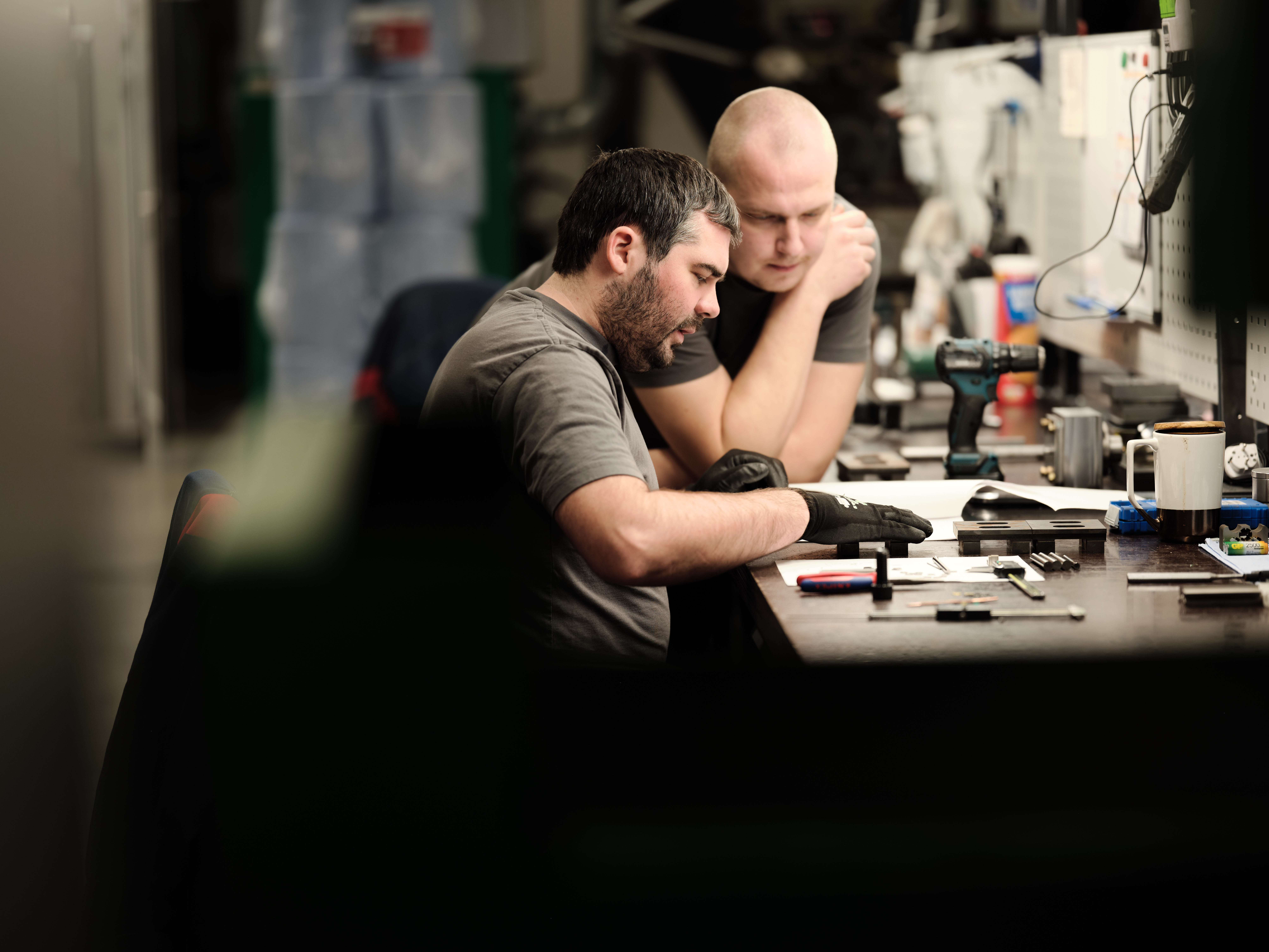 Two coworkers reviewing parts at a workbench in a workshop.
