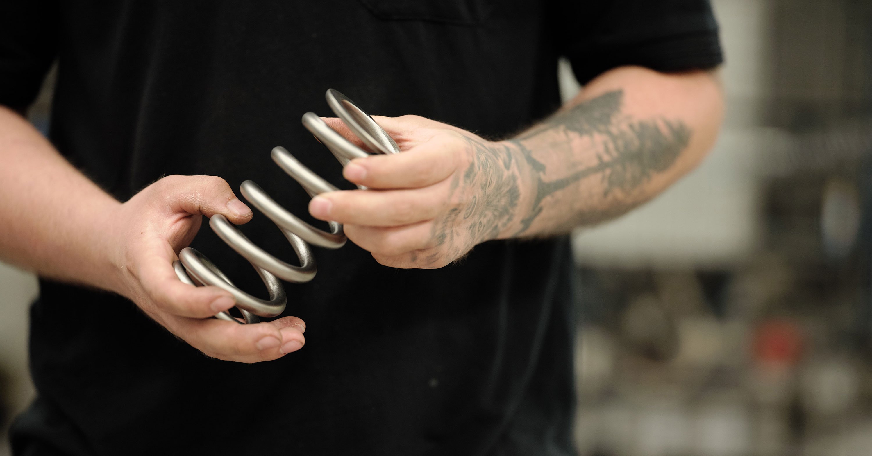 Factory worker holding a large metal coil spring in a workshop.